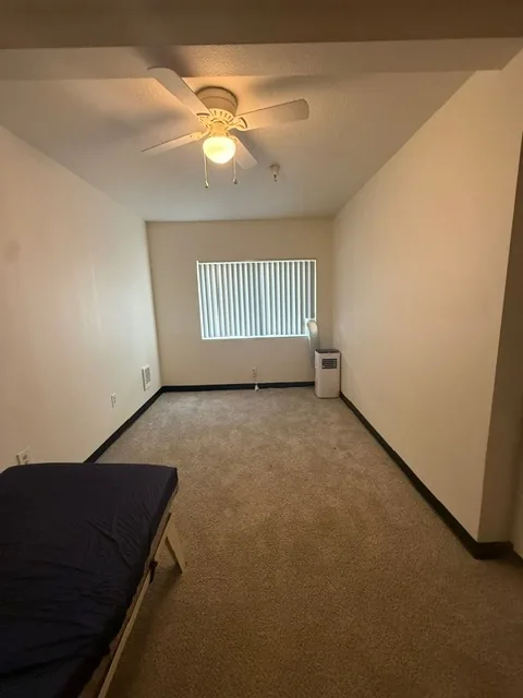 Bedroom area with window, ceiling fan, and portable air conditioner in a Barbara Maher studio