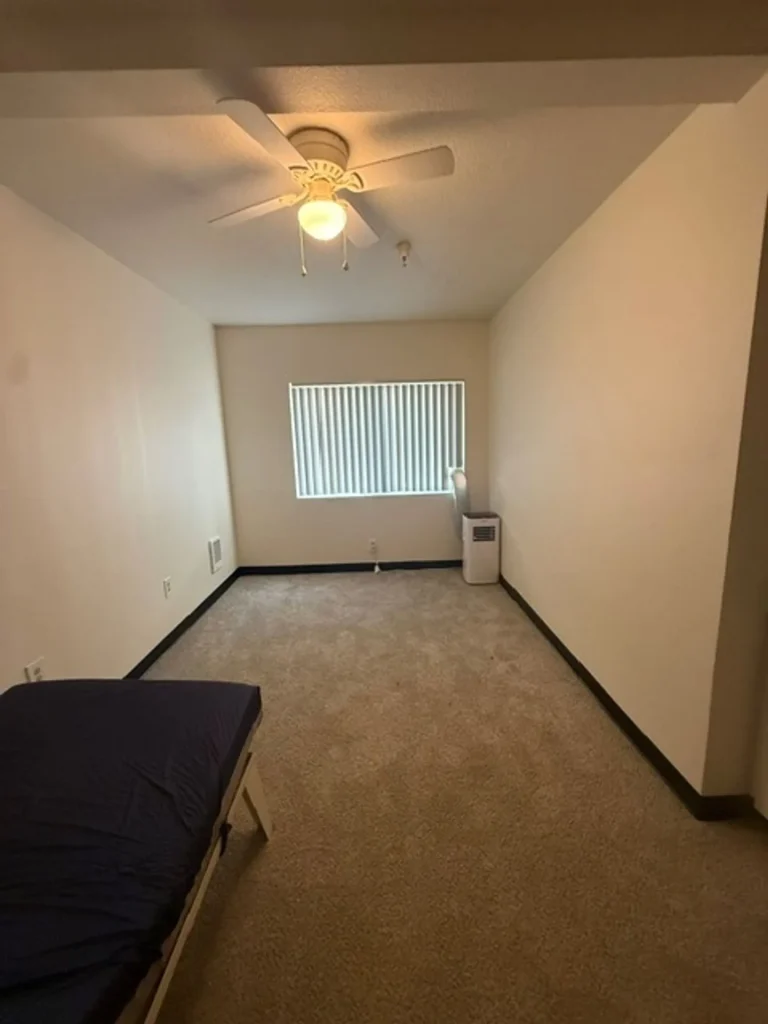 Studio bedroom area with ceiling fan and window at Barbara Maher Apartments